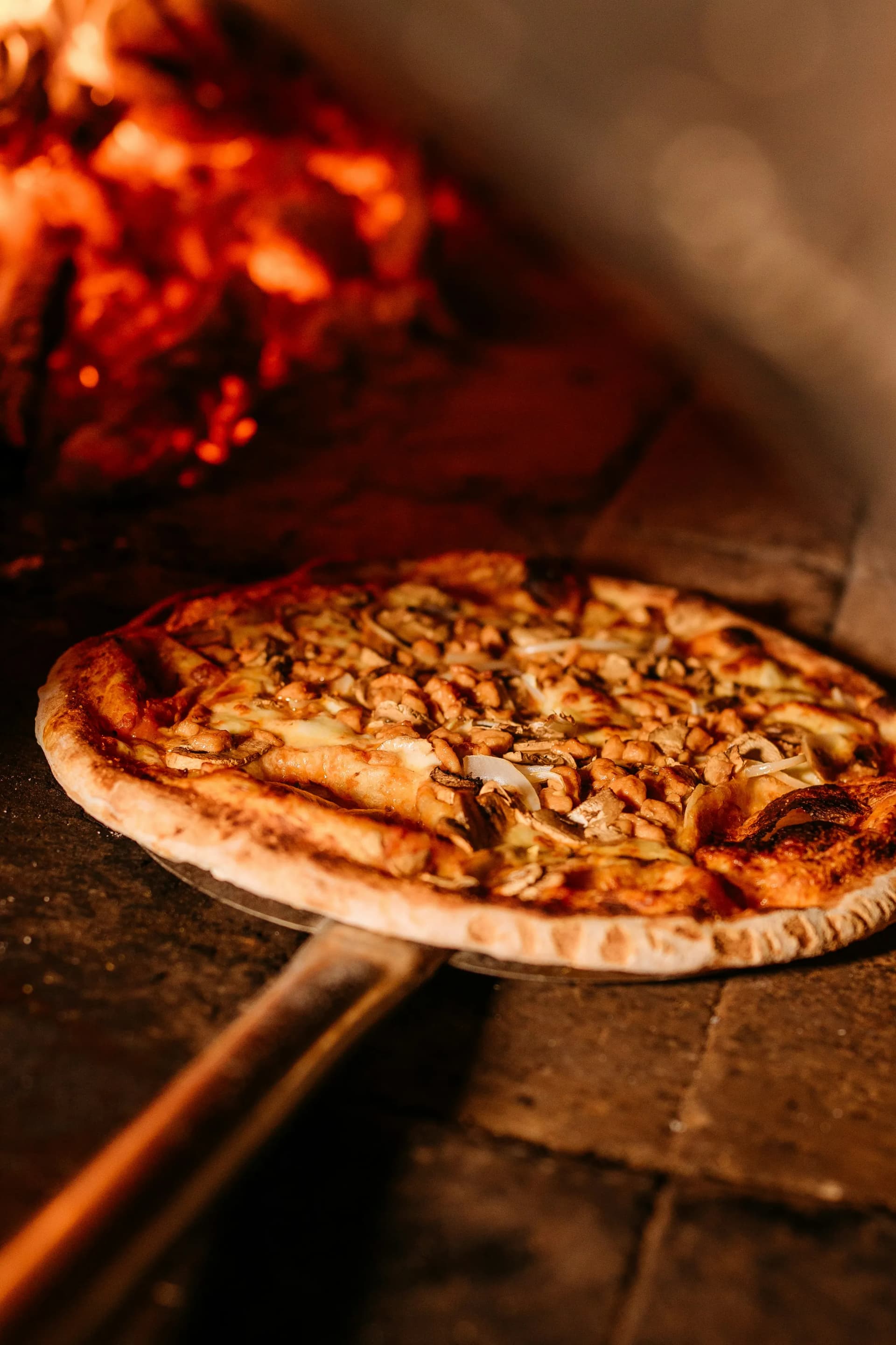 Pizza sulla pala davanti alle braci del forno a legna